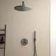 Schwarze Duscharmatur von Ideal Standard mit zentralem Bedienfeld, Kopfbrause und herausziehbarem Handbrause-Element an heller Wand, ergänzt durch ein Regal mit Pflegeprodukten.